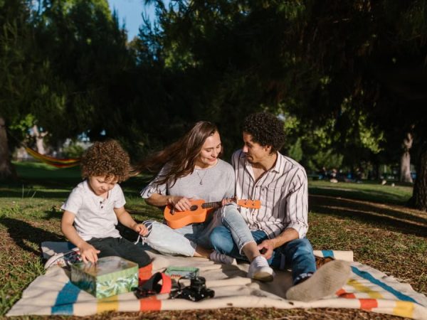 A joyful family enjoying a summer picnic with a ukulele in a sunny park setting.